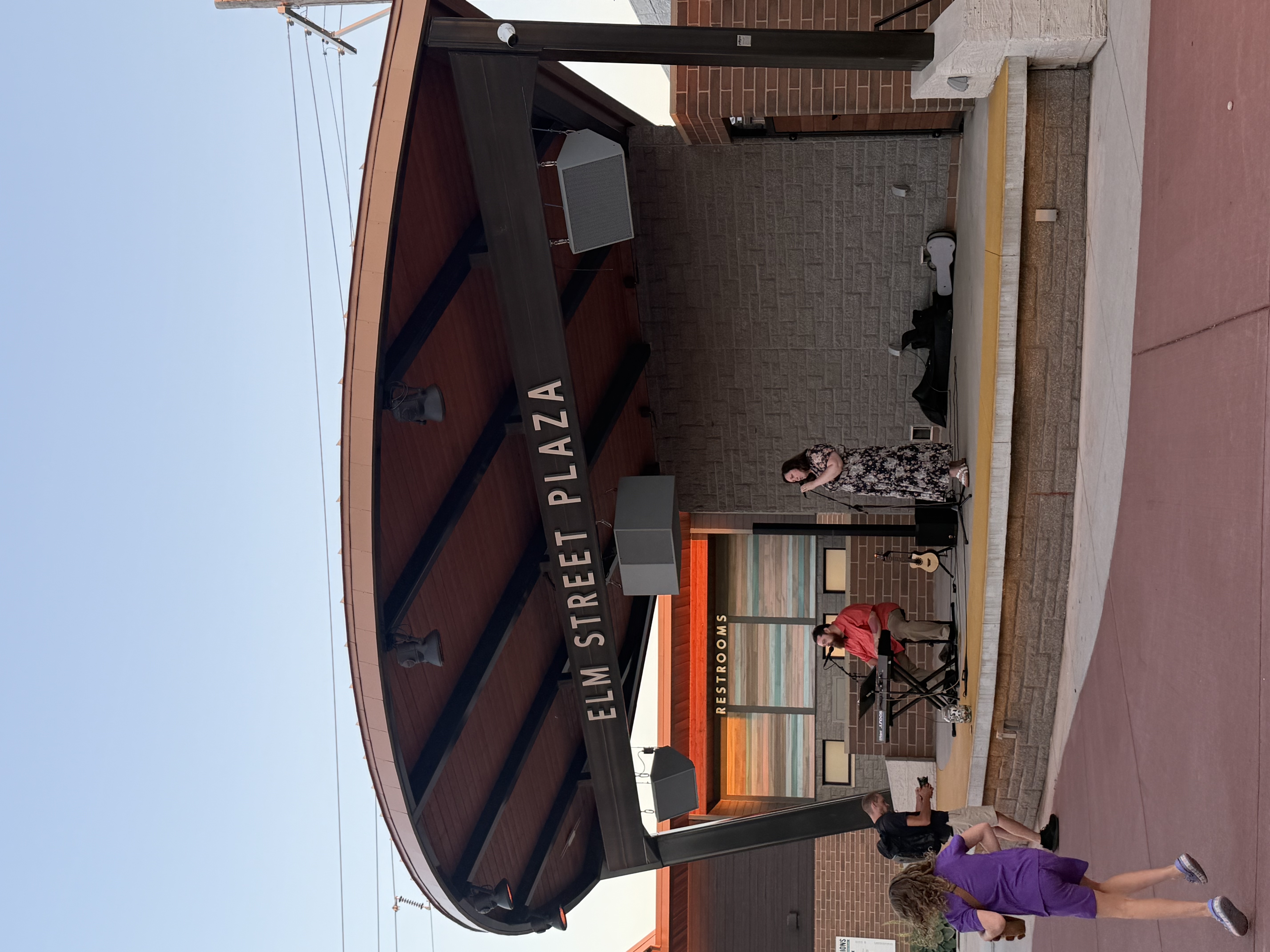 Elm Street Plaza entrance sign and shaded seating on a sunny day