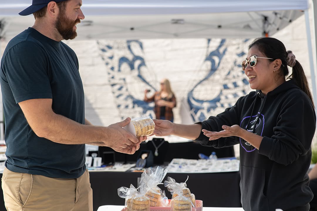 Vendor handing fresh baked goods to a customer at the market